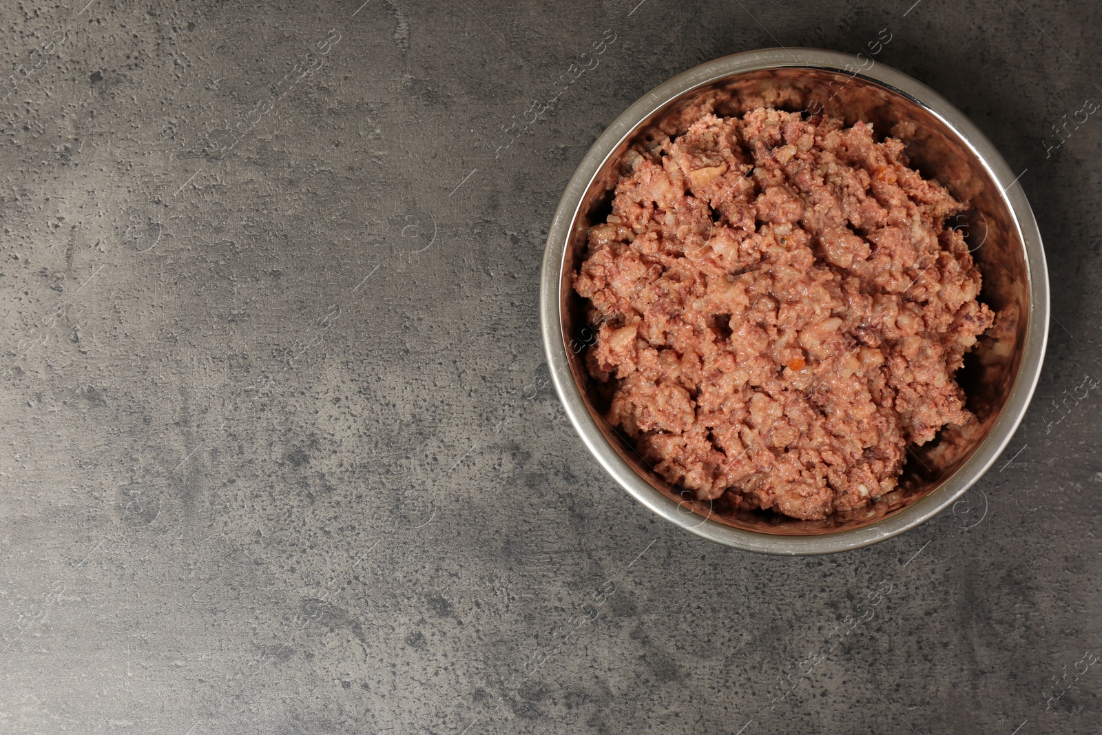 Photo of Wet pet food in feeding bowl on grey stone background, top view. Space for text