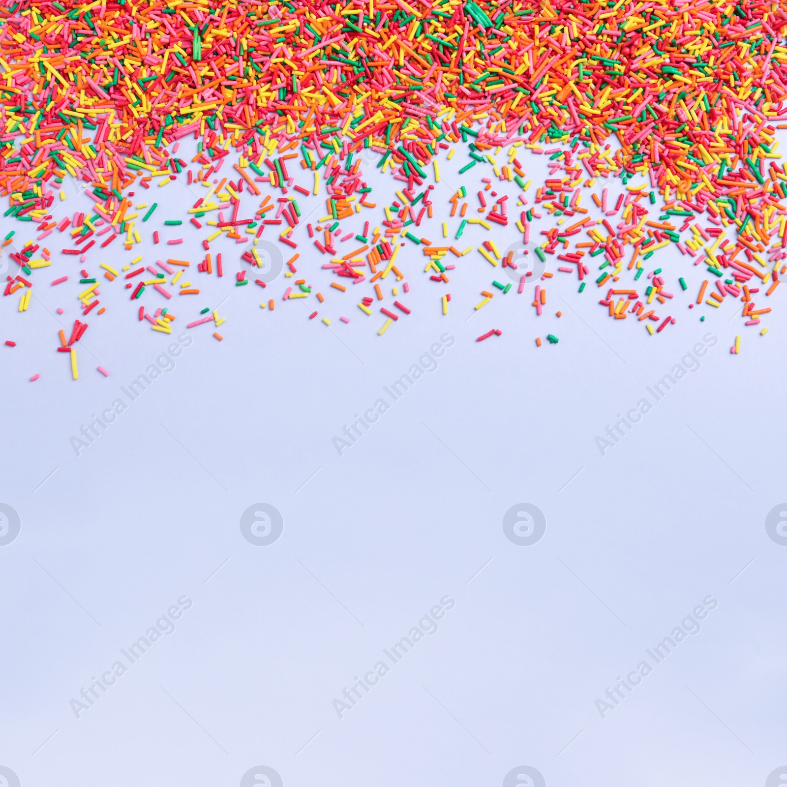 Photo of Colorful sprinkles on light grey background, flat lay with space for text. Confectionery decor