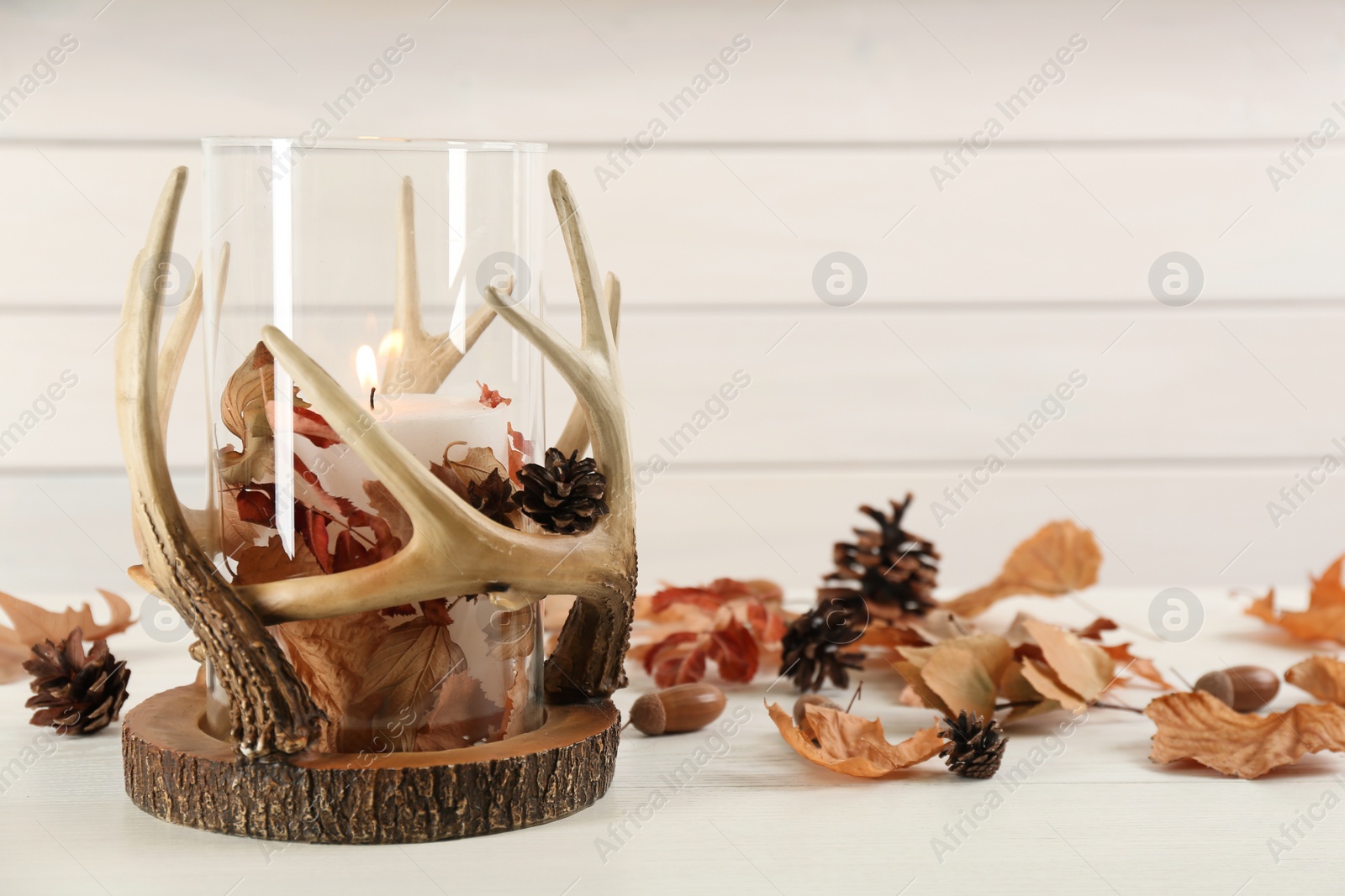 Photo of Stylish holder with burning candle and autumn decor on white wooden table. Space for text