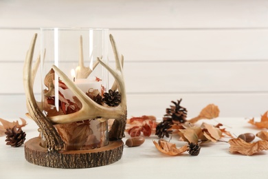 Stylish holder with burning candle and autumn decor on white wooden table. Space for text