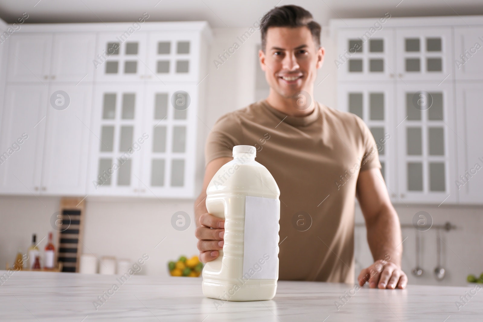 Photo of Man with gallon bottle of milk at white marble table in kitchen