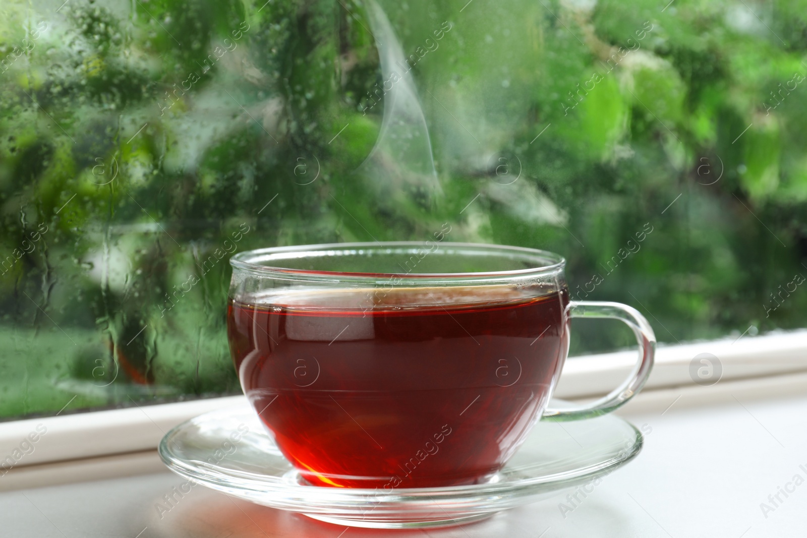 Photo of Glass cup of hot tea on windowsill. Rainy weather