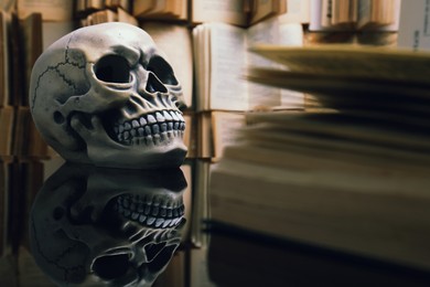 Human skull and old book on mirror table