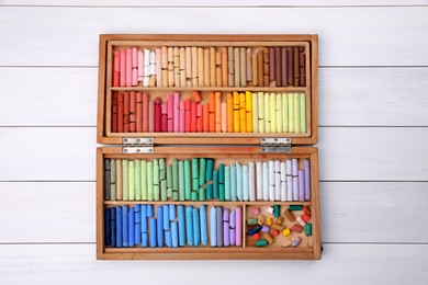 Set of soft pastels in box on white wooden table, top view. Drawing material