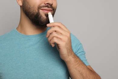 Photo of Young man applying lip balm on grey background, closeup