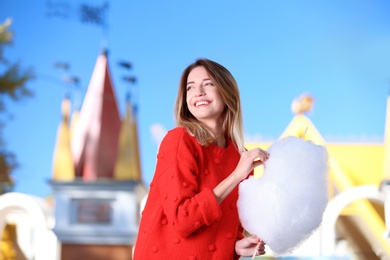 Young cheerful woman having fun with  cotton candy in amusement park