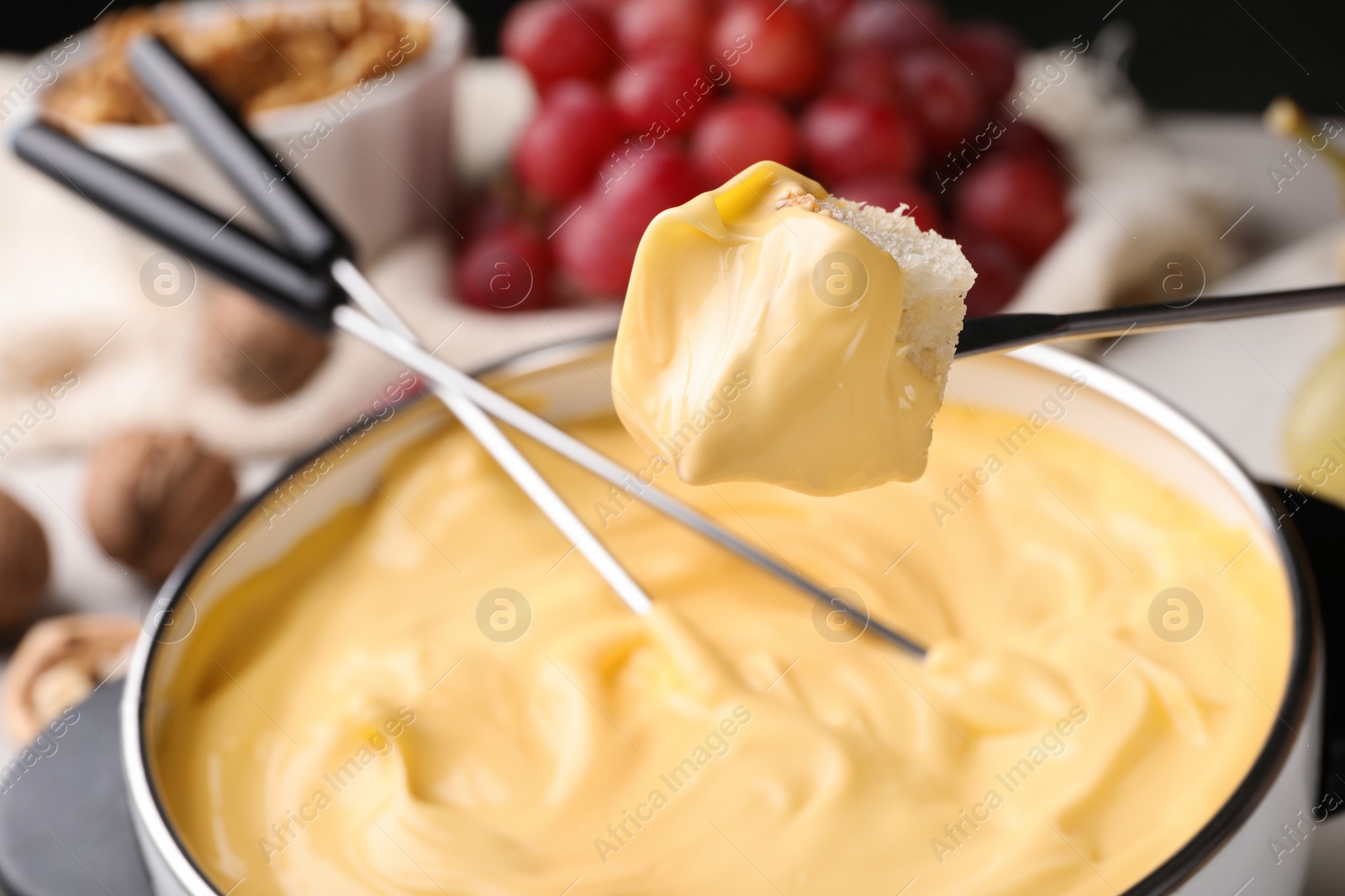 Photo of Piece of bread over pot with delicious cheese fondue on table