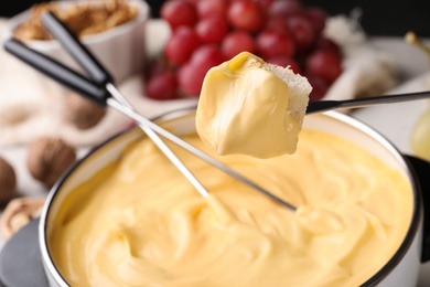 Photo of Piece of bread over pot with delicious cheese fondue on table