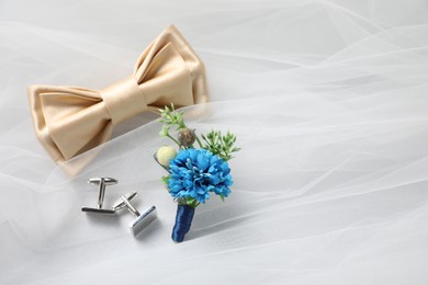 Photo of Wedding stuff. Stylish boutonniere, bow tie and cufflinks on white veil, space for text