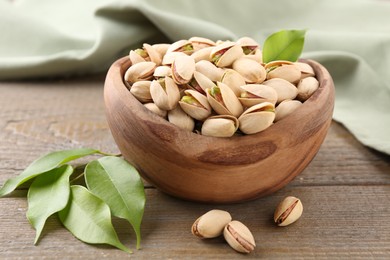 Photo of Delicious pistachios in bowl on wooden table, closeup