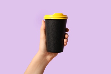 Woman holding takeaway paper coffee cup on violet background, closeup