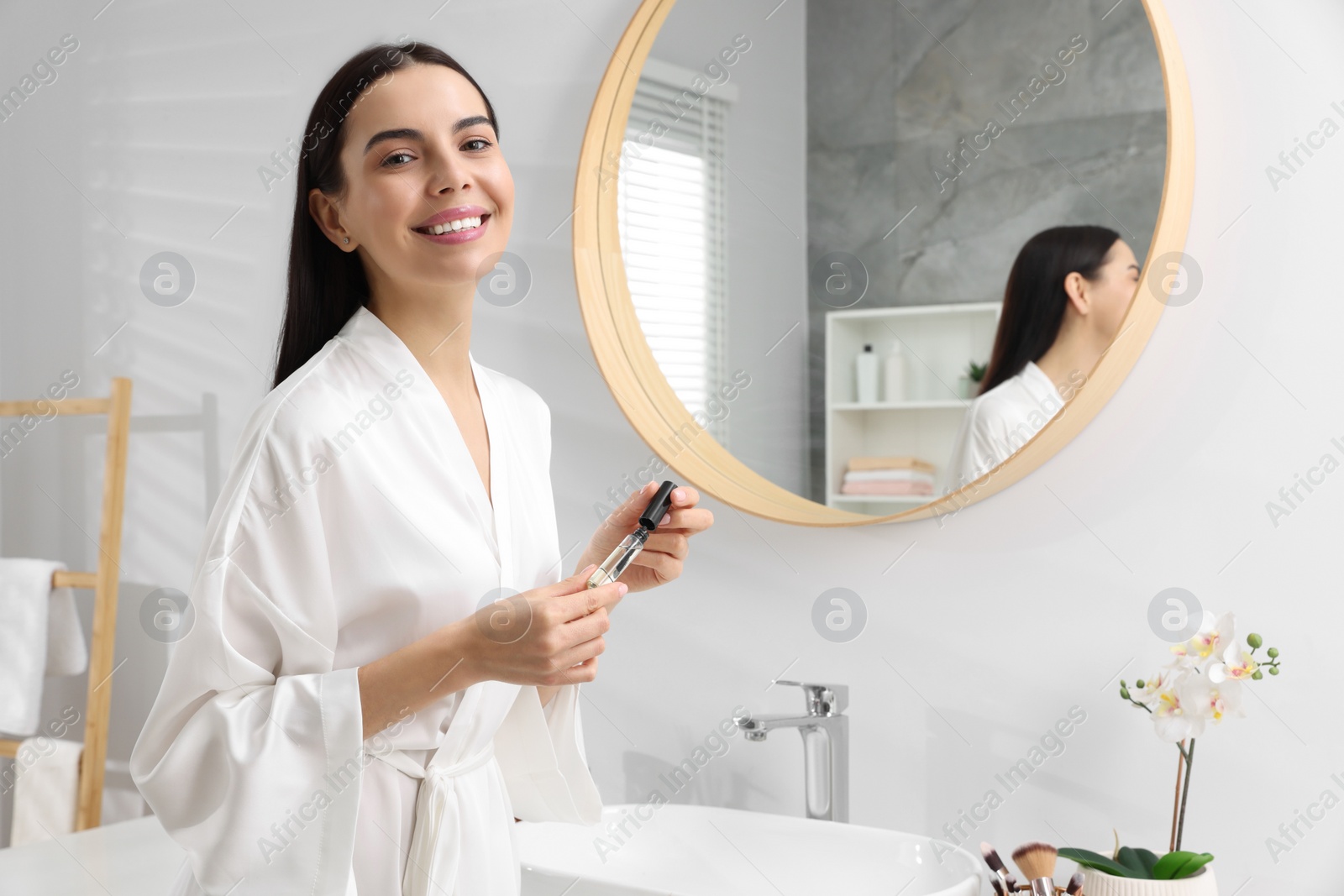 Photo of Beautiful young woman with gel for eyelashes near mirror in bathroom