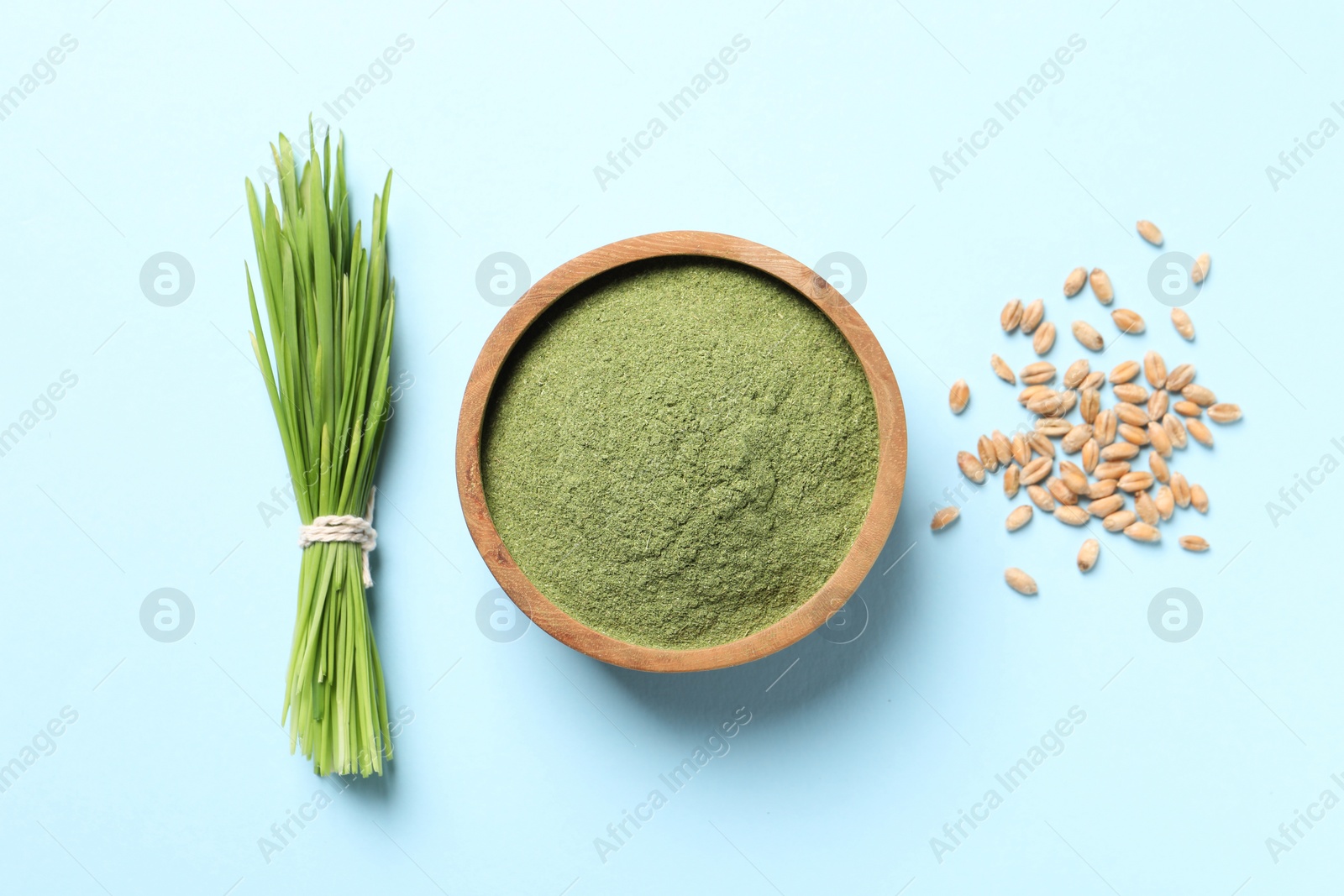 Photo of Wheat grass powder in bowl, seeds and fresh sprouts on light blue background, flat lay