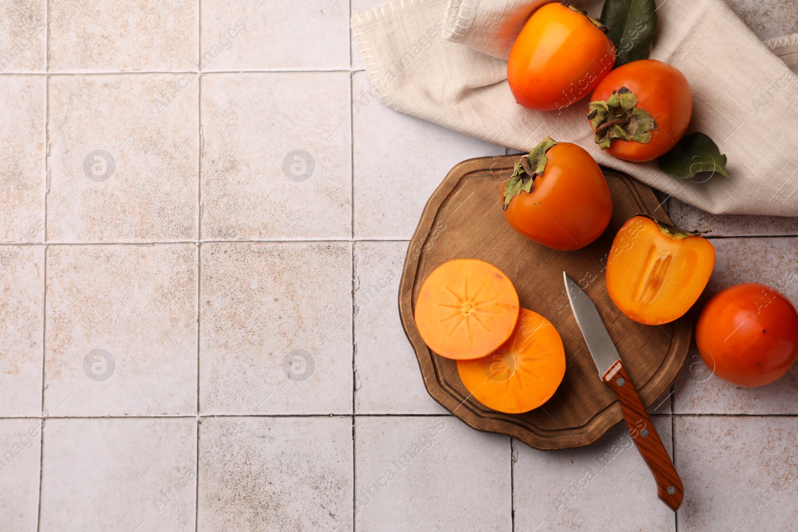 Photo of Delicious ripe juicy persimmons and knife on tiled surface, flat lay. Space for text