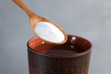 Photo of Spoon with baking soda over glass of water on grey background, closeup