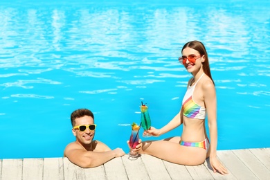 Happy young couple with cocktails resting at swimming pool