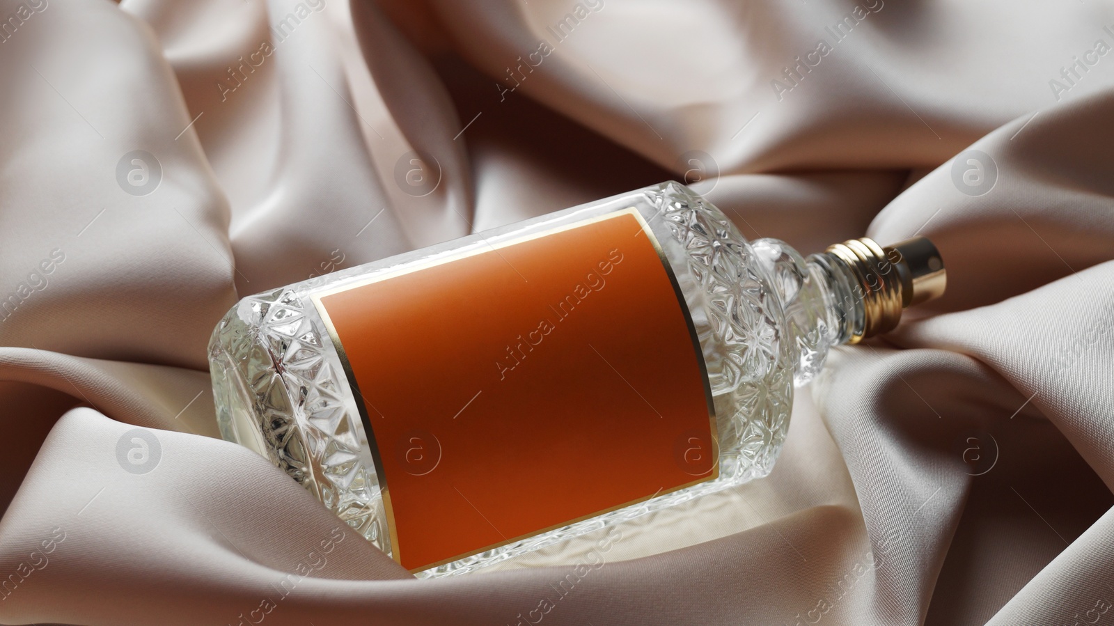 Photo of Luxury bottle of perfume on beige silk, closeup