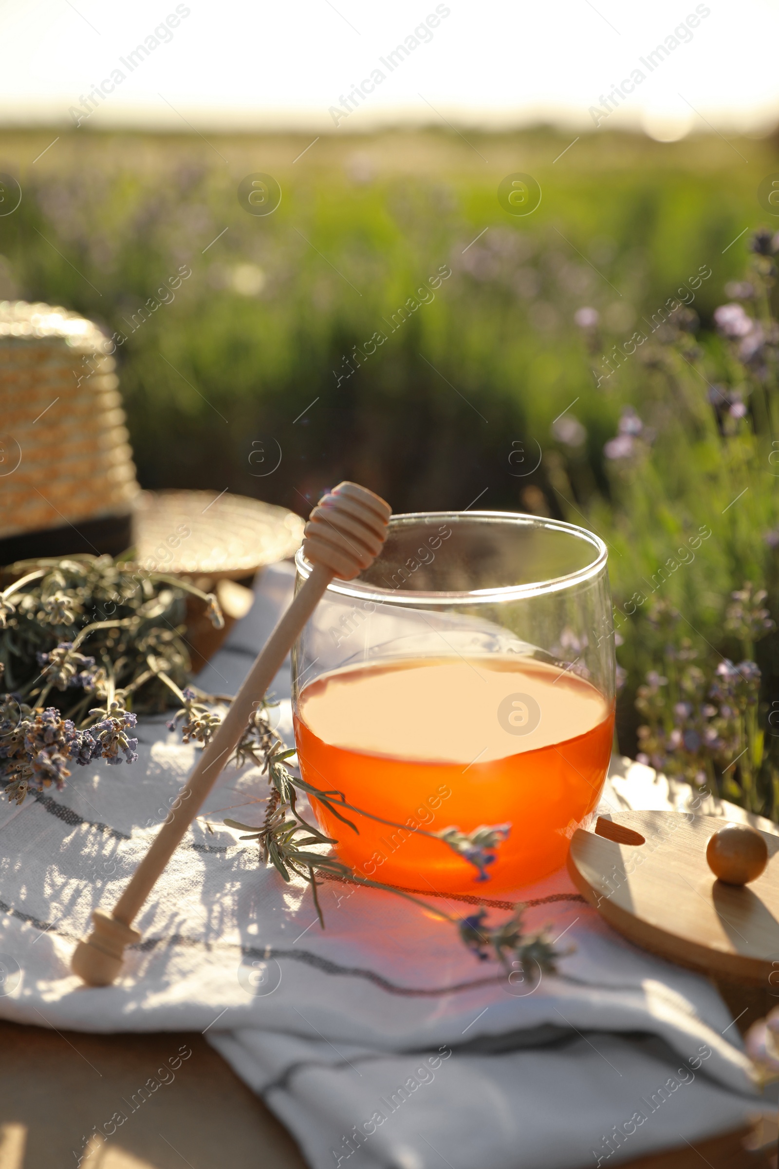 Photo of Jar of honey on wooden table in lavender field