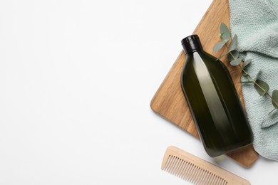 Bottle of shampoo, comb and green branch on white table, flat lay. Space for text