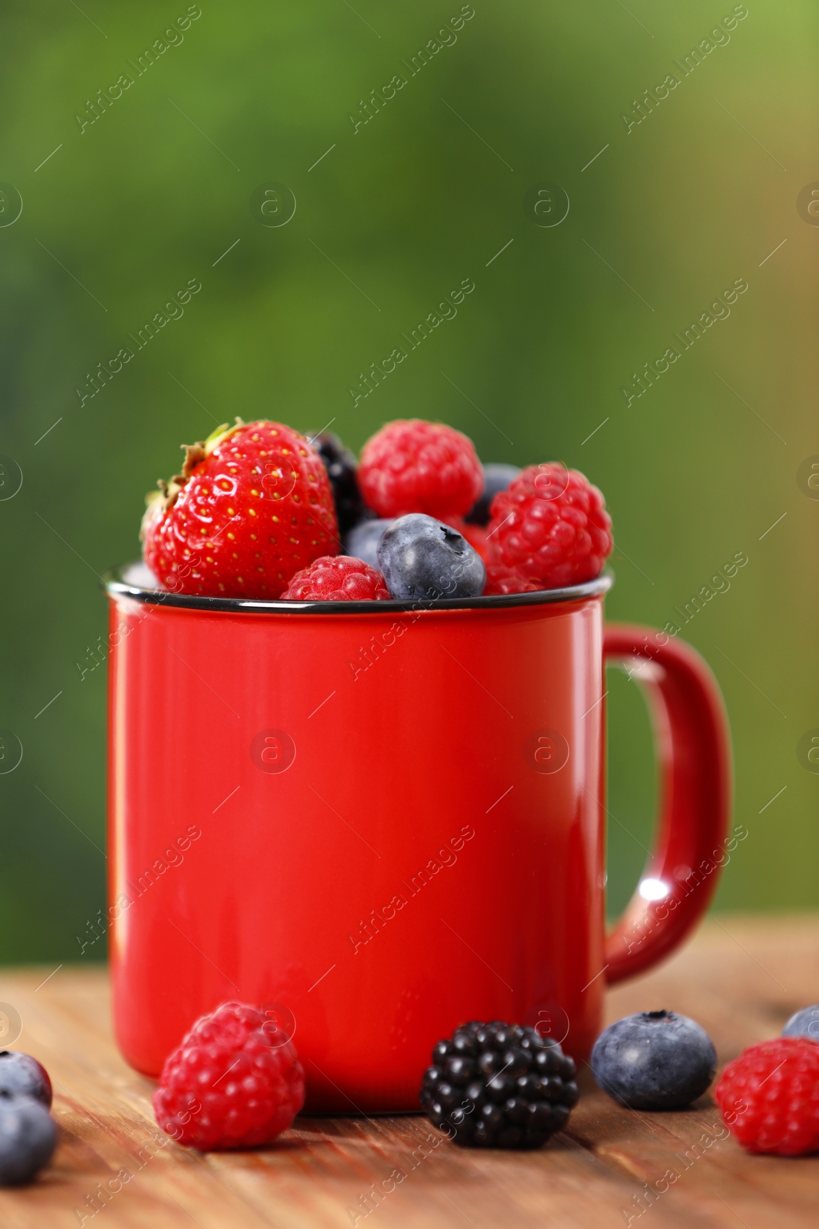 Photo of Mug with different fresh ripe berries on wooden table outdoors