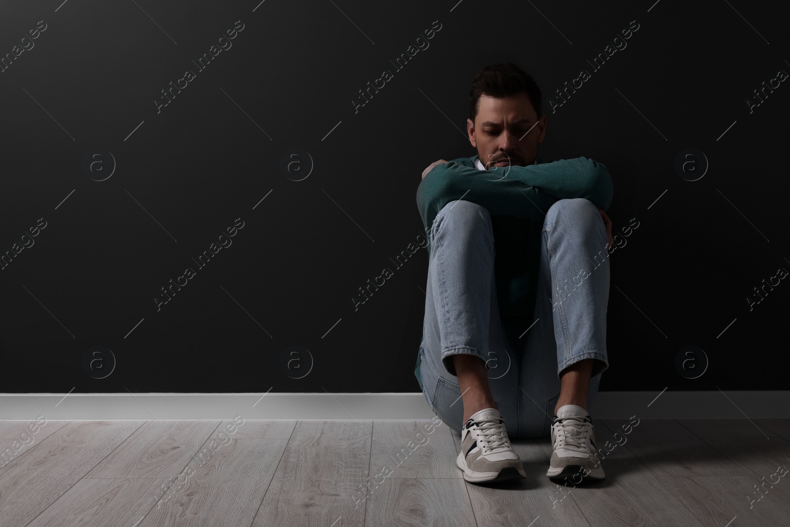 Photo of Upset man sitting on floor near black wall. Space for text