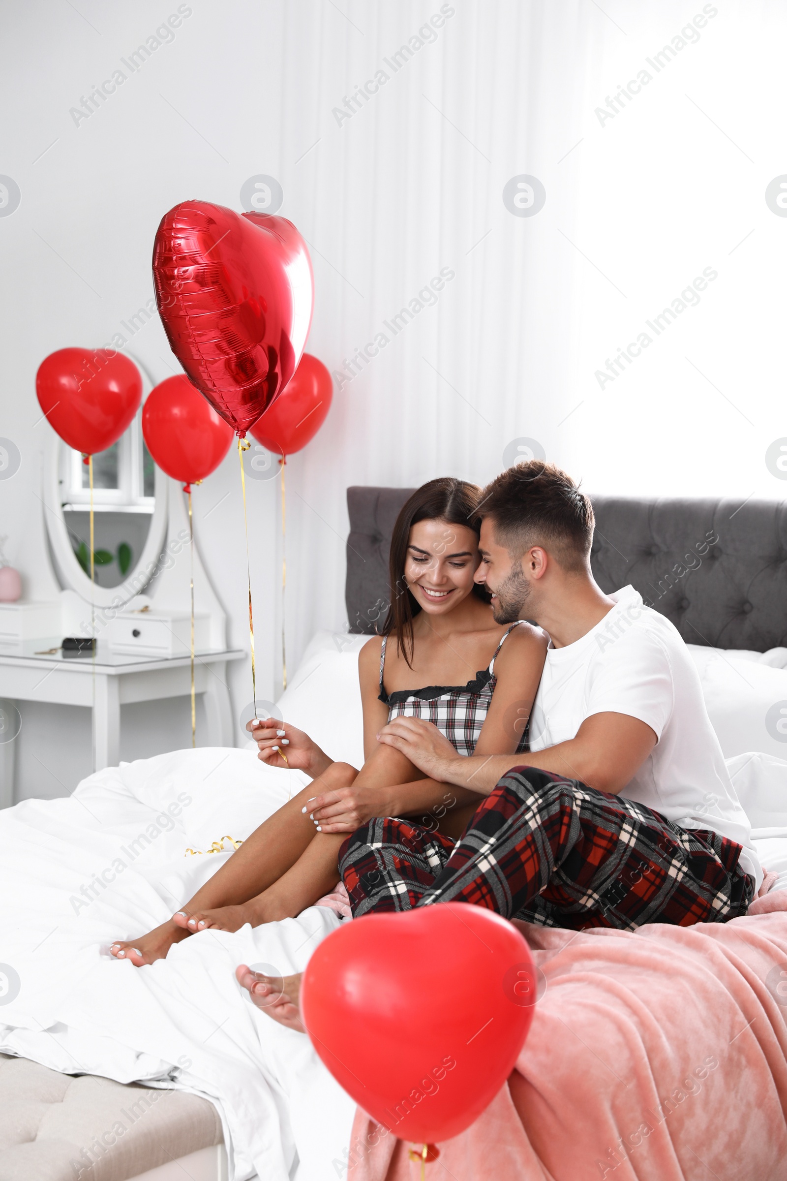 Photo of Young couple in bedroom decorated with air balloons. Celebration of Saint Valentine's Day