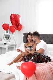 Photo of Young couple in bedroom decorated with air balloons. Celebration of Saint Valentine's Day