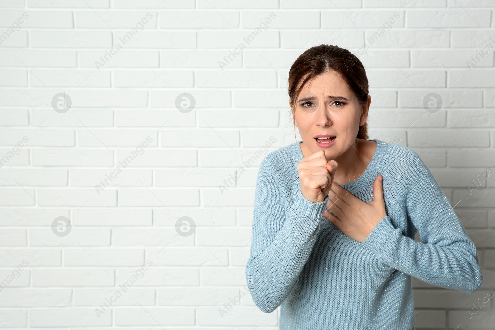 Photo of Woman suffering from cough near brick wall. Space for text