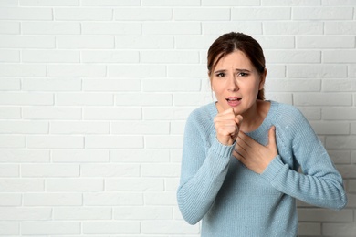 Woman suffering from cough near brick wall. Space for text