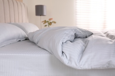 Comfortable bed with soft blanket indoors, closeup