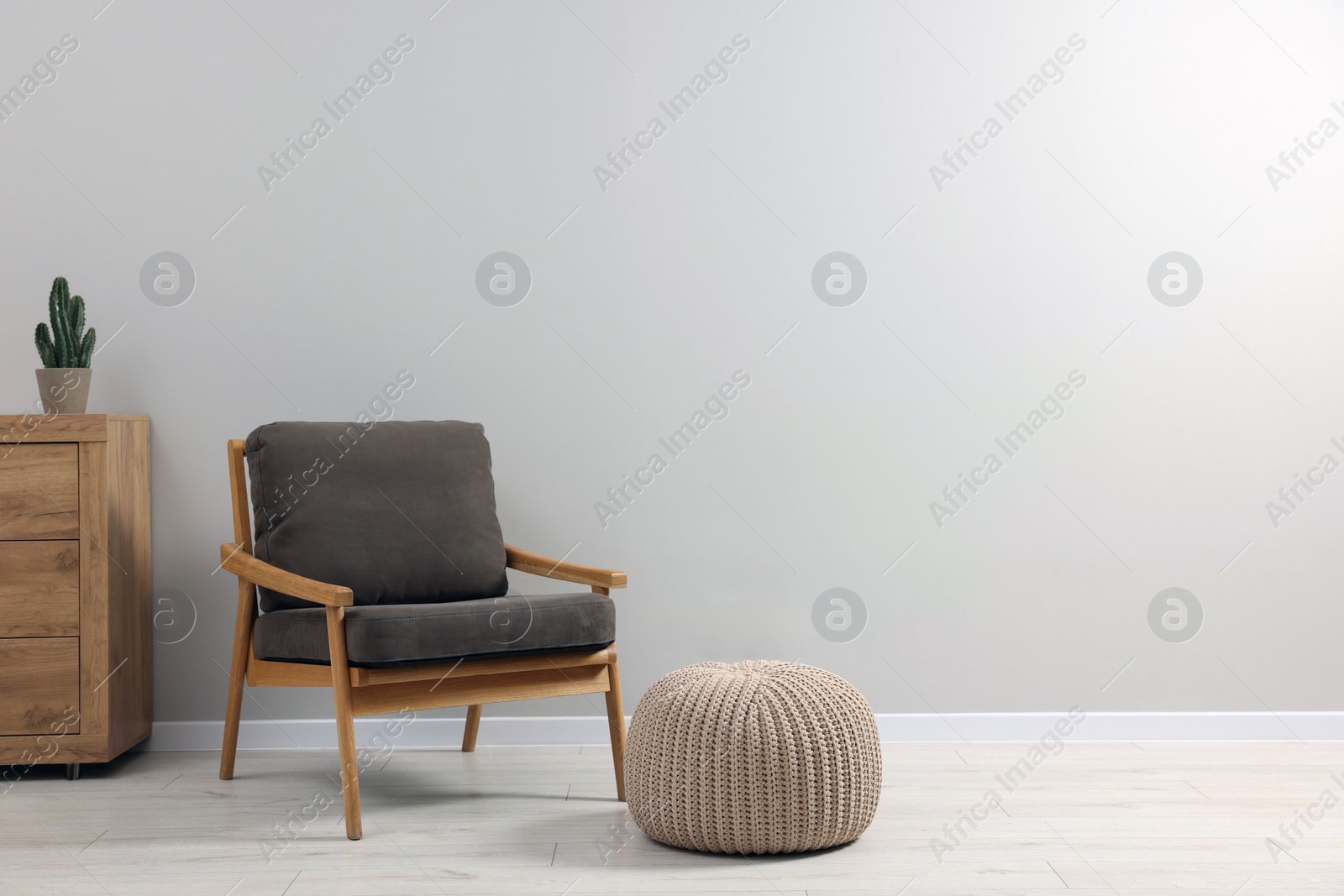 Photo of Comfortable armchair, chest of drawers and pouf near light grey wall indoors, space for text. Interior design