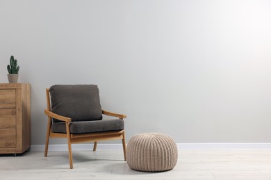 Comfortable armchair, chest of drawers and pouf near light grey wall indoors, space for text. Interior design