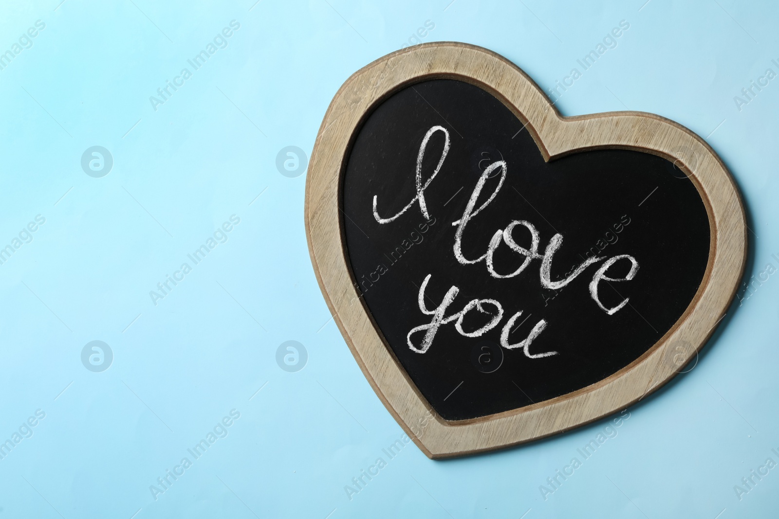 Photo of Heart shaped chalkboard with words I Love You on light blue background, top view. Space for text