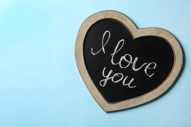 Heart shaped chalkboard with words I Love You on light blue background, top view. Space for text