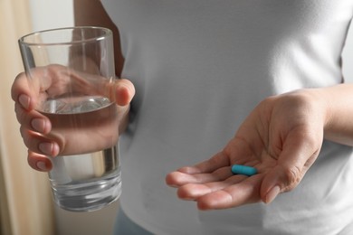 Woman with glass of water and pill on blurred background, closeup