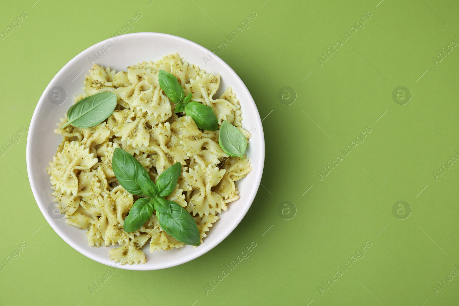 Photo of Delicious pasta with pesto sauce and basil on light green background, top view. Space for text