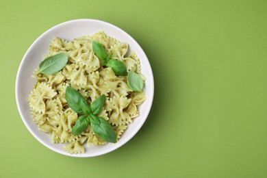 Delicious pasta with pesto sauce and basil on light green background, top view. Space for text