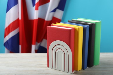 Learning foreign language. Different books on wooden table near flag of United Kingdom, space for text