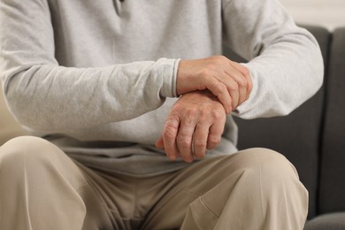 Senior man suffering from pain in hand indoors, closeup. Rheumatism symptom