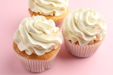 Photo of Tasty vanilla cupcakes with cream on pink table, closeup