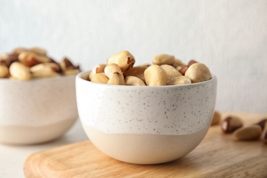 Photo of Bowl with tasty Brazil nuts on wooden board