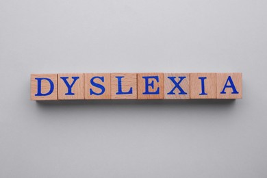 Wooden cubes with word Dyslexia on light grey background, flat lay