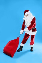 Full length portrait of Santa Claus pulling sack on light blue background
