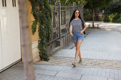 Beautiful young woman in stylish sunglasses walking on city street