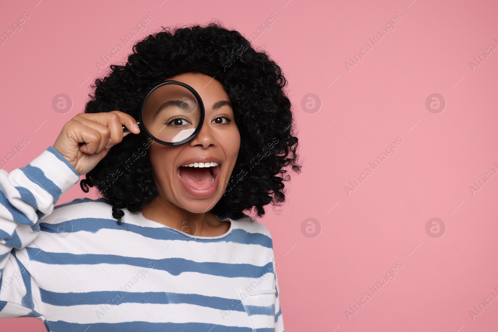 Photo of Emotional woman looking through magnifier glass on pink background, space for text