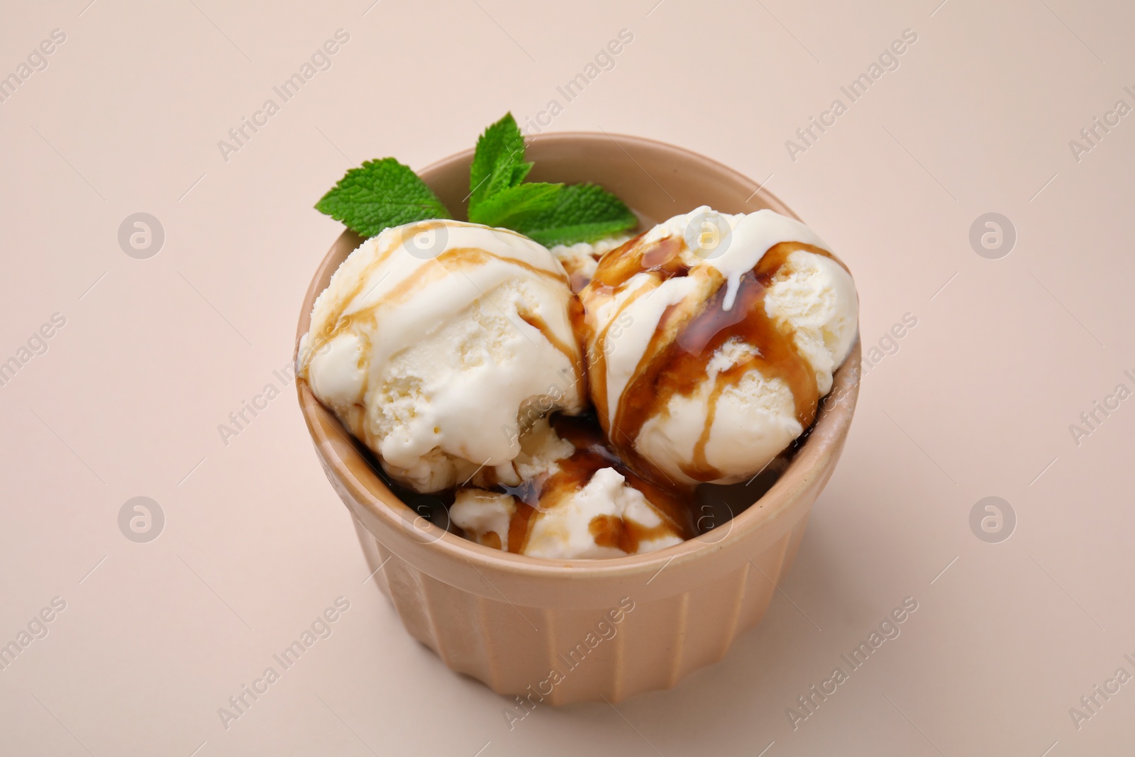 Photo of Scoops of ice cream with caramel sauce and mint leaves on beige table, closeup