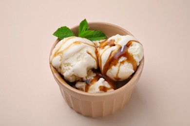 Photo of Scoopsice cream with caramel sauce and mint leaves on beige table, closeup
