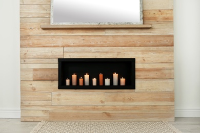 Photo of Burning candles on shelf in wooden wall indoors