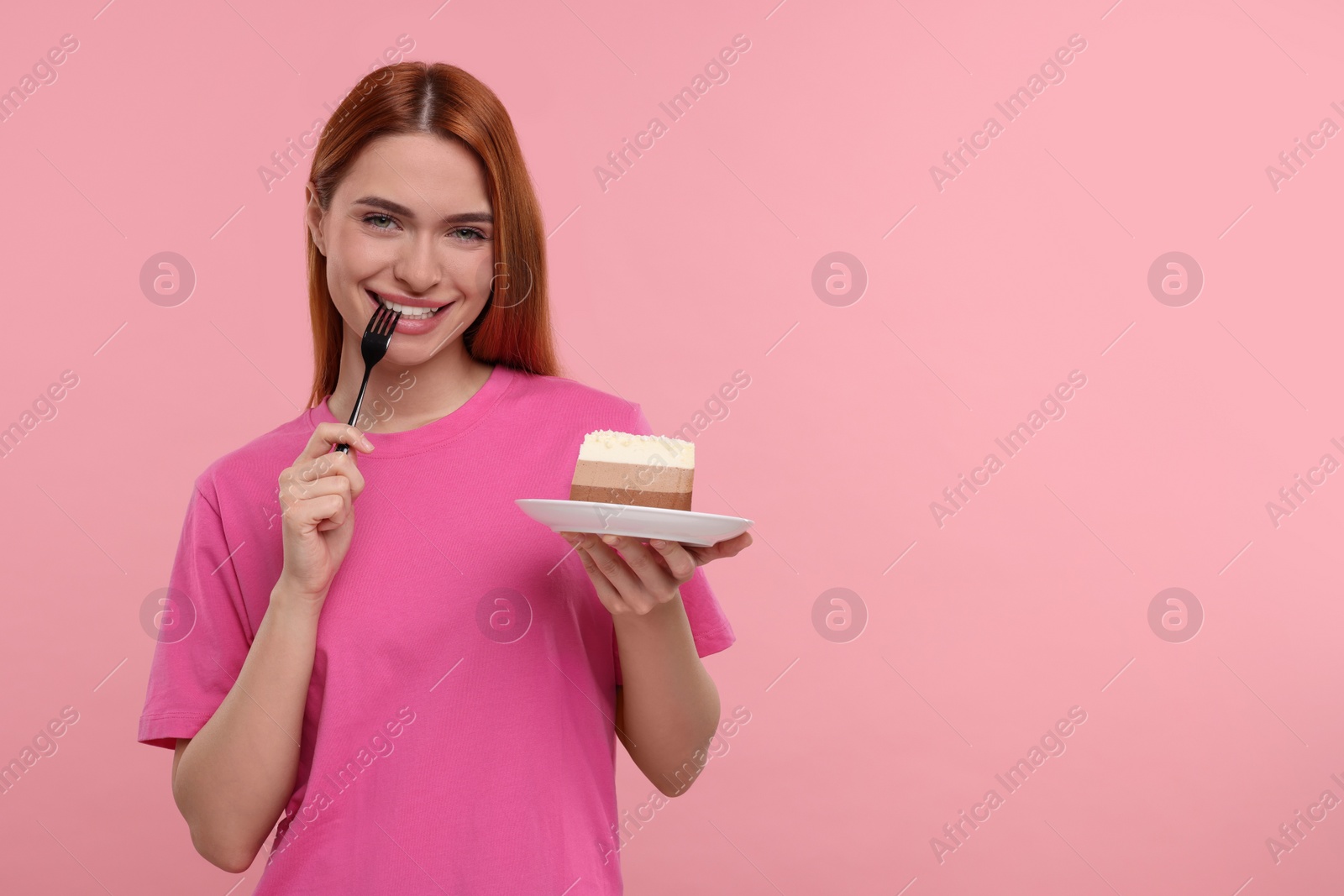 Photo of Young woman eating piece of tasty cake on pink background, space for text