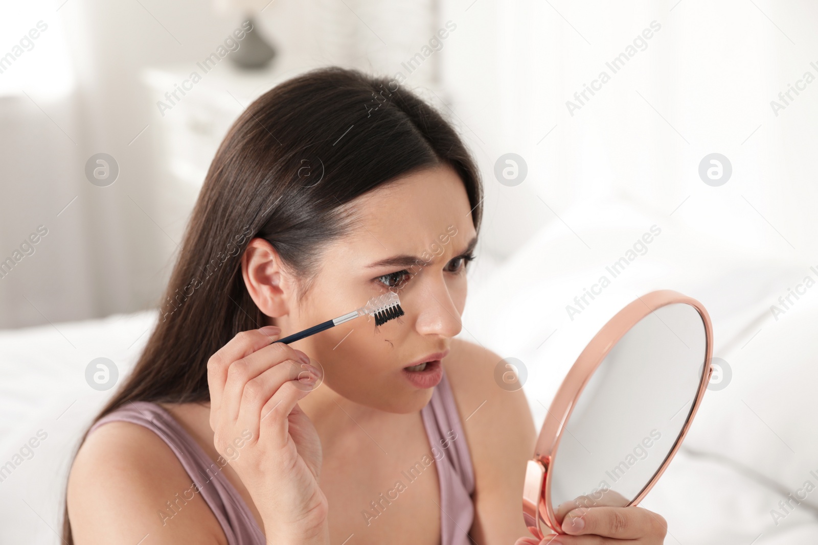 Photo of Beautiful woman with fallen eyelashes and cosmetic brush looking into mirror indoors